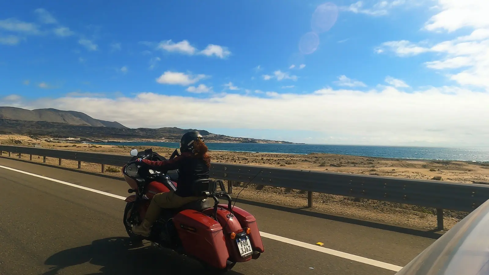 Joelma pilotando sua Harley-Davidson na estrada costeira com o Oceano Pacífico ao fundo