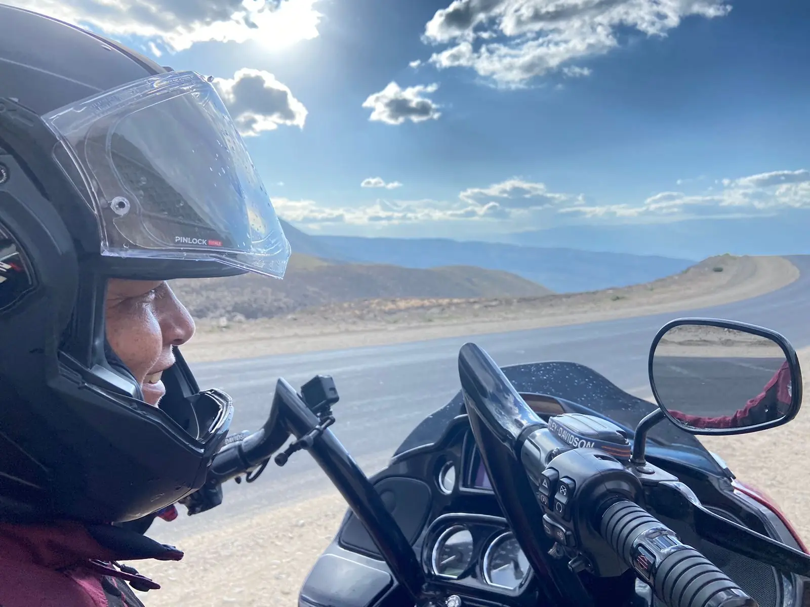 Joelma na Harley-Davidson em trecho de serra com montanhas e sol ao fundo
